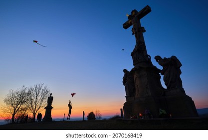 Silhouettes of kids flying kites with stone christianity monument in the foreground at sunset - Shutterstock ID 2070168419