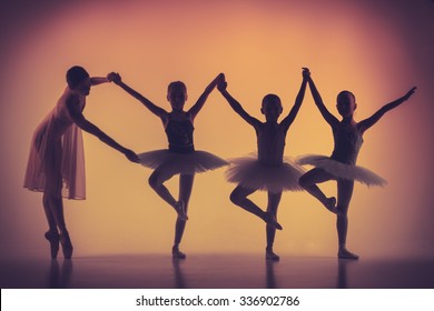 The silhouettes of little ballerinas with personal ballet teacher in dance studio posing on a orange background - Powered by Shutterstock