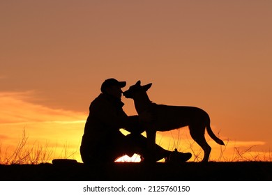 Silhouettes of a man and a dog on a sunset background, the owner walks with his pet in nature, Belgian Shepherd Malinois dog - Powered by Shutterstock