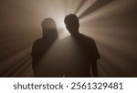 Silhouettes of man and woman hugging and walking towards camera against bright warm colored spotlight, isolated on studio background close up shot.