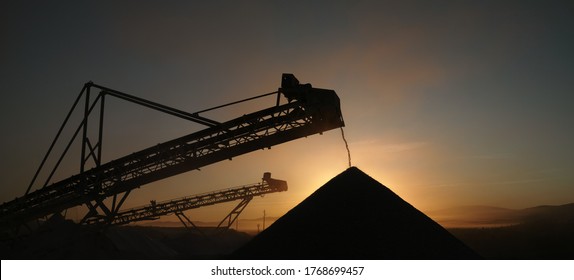 Silhouettes of metal structures of stone crushing equipment at a mining plant against the backdrop of sunrise, panorama.