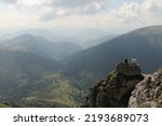 Silhouettes of mountains in a noon light. Dark silhouettes of peaks under the blue sky. Two yound man sitting on a rock in the front. Peaks of Mala fatra in Slovakia. View from the top to the valley.