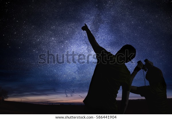 Silhouettes of people observing stars in night\
sky. Astronomy\
concept.