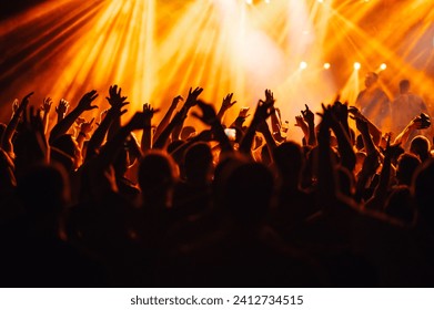 Silhouettes of people rising their hands and having fun at the music open air festival. Nightlife. People dancing at rock concert and going wild. There are orange stage lights. On stage are musicians. - Powered by Shutterstock