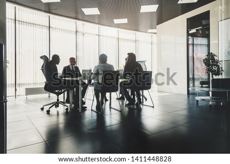 Silhouettes of people sitting at the table. A team of young businessmen working and communicating together in an office. Corporate businessteam and manager in a meeting.