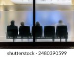 Silhouettes of people sitting in a waiting room with frosted glass, showcasing anonymity and patience while waiting.