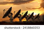 Silhouettes of radar antennas receivers on the ground in the mountains against sunset sky. Few of large satellite stations in the field turned up.