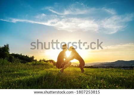 Silhouettes of runner and dog on field under golden sunset sky in evening time. Outdoor running. Athletic young man with his dog are funning in nature.