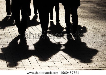 Silhouettes and shadows of people on the city street. Crowd walking down on sidewalk, concept of strangers, crime, society, gang or population