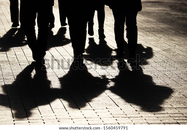 Silhouettes and shadows of people on the city\
street. Crowd walking down on sidewalk, concept of strangers,\
crime, society, gang or\
population