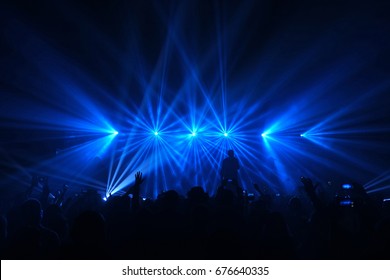 Silhouettes of singer standing on the stage under the blue spotlight flare rays and silhouettes of people in the foreground