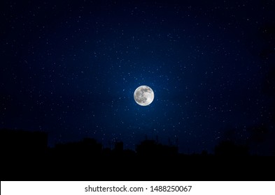 Silhouettes of skyscrapers different construction in the dark town with background of a large moon and clouds at nighttime. - Shutterstock ID 1488250067