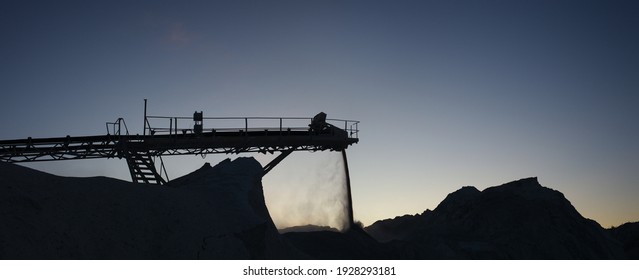 Silhouettes of structures of working stone crushing equipment at a mining plant, evening panorama against the background of a blue sky.  Mining industry.