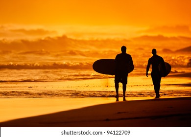 Silhouettes Of Surfers On The Beach At Sunset