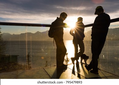 Silhouettes of three friends and a cat standing on a glass balcony above the sea looking at the sunset 