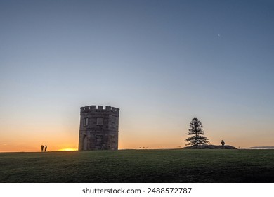 Silhouettes of three people enjoying the sunset by the La Perouse Macquarie Watchtower, in Randwick, Sydney, Australia. A couple on the left and a sole guy on the right. - Powered by Shutterstock
