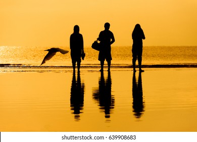 Silhouettes Of Three People Standing And Bird In Ocean At Sunrise