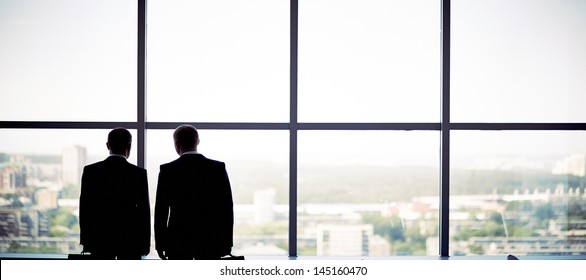 Silhouettes Of Two Businessmen Standing By The Window