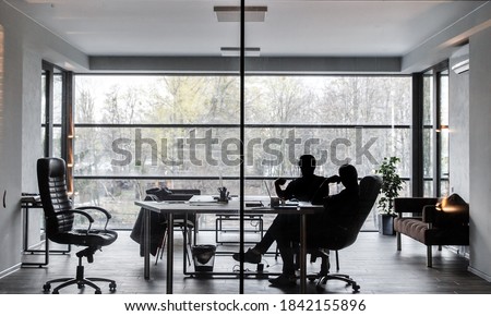 Silhouettes of two men, they are sitting in an office