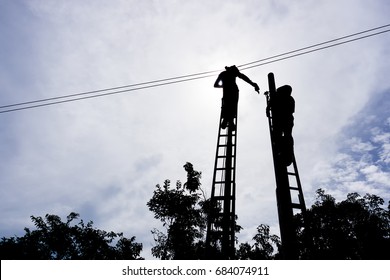 Silhouettes of two men working on electrical/telecommunication cable.