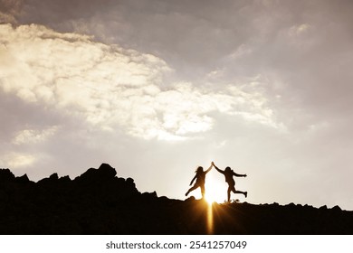 Silhouettes of two people jumping on a rocky hill at sunset. Joyful silhouettes against a dramatic sky. Energetic jump, rocky hill, and sunset glow. Hiking adventure on mountain trail. - Powered by Shutterstock