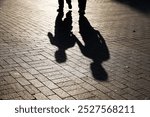 Silhouettes of two people walking down the street. Shadows of adult and child on pavement