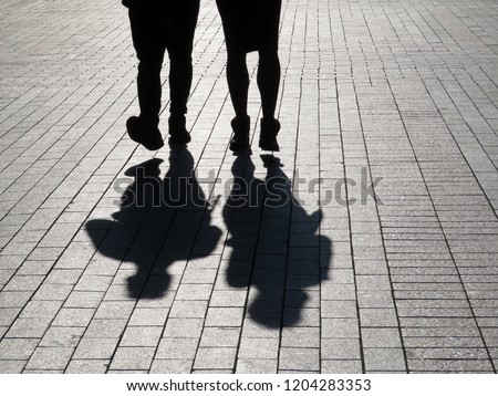Silhouettes of two people walking down the street. Couple outdoors, people shadows on pavement, concept for dramatic stories