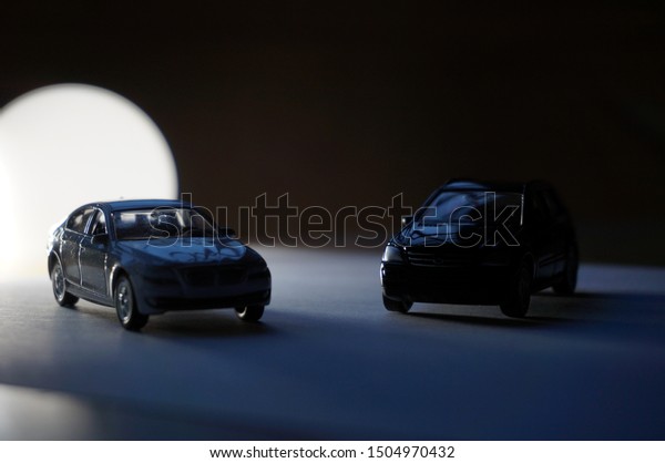 Silhouettes of two scale models of a sedan car\
and a SUV 4×4 all terrain vehicle in the dark, with white light,\
shadows and clair-obscur\
effects