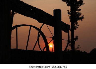 Silhouettes of wagon wheels and wood fence with orange sunset