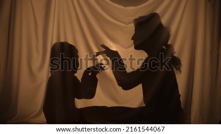 Silhouettes of woman and boy telling stories using shadow play and depicting flying birds with hands. Mom and little son have fun, sitting behind curtain at home. Puppet theater of shadows. Close up.