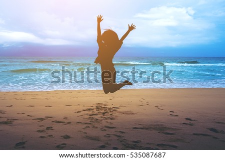 Silhouettes of a woman jumping on the beach in front of ocean with feeling happy and freedom
