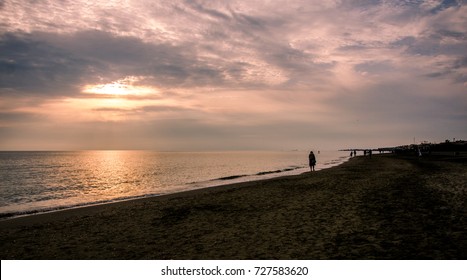 Silhouettes Of Woman Walking On Sandy Beach At Sunset, Lido Di Ostia, Rome, Italy
