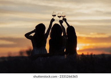 Silhouettes of women in the park in evening sunlight. The lights of a sun. The company of female friends enjoys a summer picnic and raise glasses with wine. Copy space.	
 - Shutterstock ID 2331266365