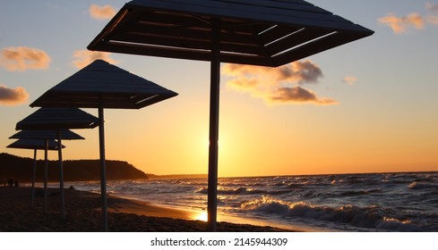 Silhouettes of wooden beach umbrellas on wet sand in stormy weather at summer sunset  - Powered by Shutterstock