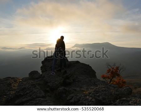 Silhouettes of young couple standing on a mountain and looking to each other on beautiful sunset background. Love of guy and girl. 