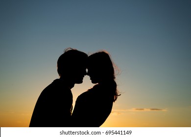 Silhouettes of a young girl and her boyfriend embraces against a blue sky with clouds in sunset sun.Copy space.Magic moments of loving hearts. Lovers in nature. Lovers silhouette.Happy Family Outdoor
