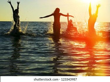 Silhouettes of young group of people jumping in ocean at sunset