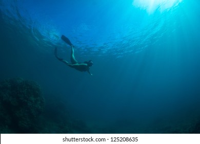 Silhouettes Of A Young Women Free Diving In The Pacific Ocean