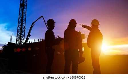 SilhouetteTeams Businessman engineer looking blueprint in a building site over Blurred construction site at sunset