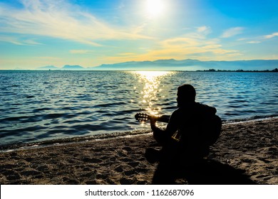 Silhouette.Young Men Playing Guitar While Sitting On The Beach.