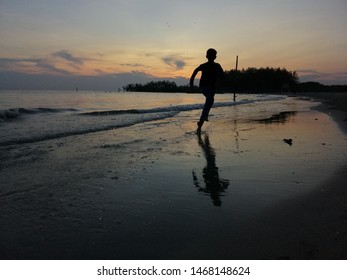 A Silhoutte Of A Boy Running On A Beach At Sunset