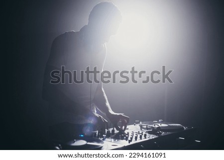 Silhoutte of a club DJ mixing vinyl records on stage. Disc jockey playing music on a concert in night club