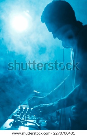 Silhoutte of club dj playing techno music set in smoke and blue lights