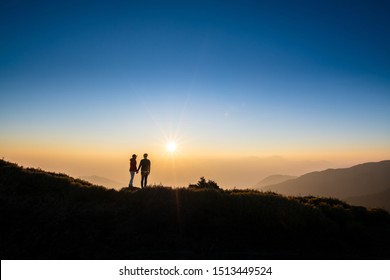 Silhoutte of a couple hold hand of each other looking at sunset on top of hill with background of mountain and golden color of sunshine. Concept of teamwork, successful. - Powered by Shutterstock