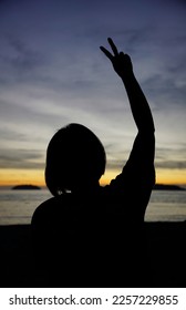 Silhoutte of a girl with peace sign in the background of sunset in Kinabalu Island, Malaysia                                