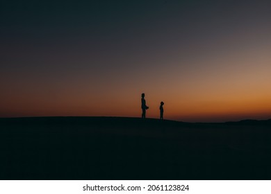 silhoutte of a mother and child standing in front of the orange sky during late dusk