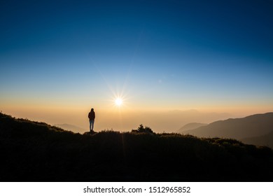 Silhoutte of woman standing on top of the mountain looking at sunset. Concept of successful, discover, wanderlust.