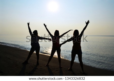 Silhuette of three ladies having fun with sunrise on the beach
