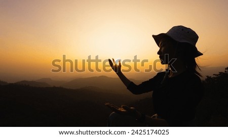 Silhuette Young Woman praying on the mountain, arms outstretched observing a beautiful dramatic sunrise.  