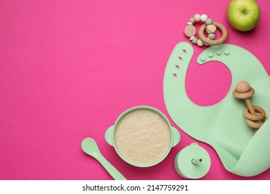 Silicone baby bib, toys and plastic dishware with healthy food on pink background, flat lay. Space for text - Shutterstock ID 2147759291